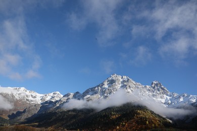 Picturesque landscape of high mountains covered with thick mist under blue sky on autumn day