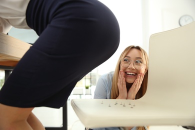 Young woman putting pins on chair while her colleague sitting down in office, closeup. Funny joke