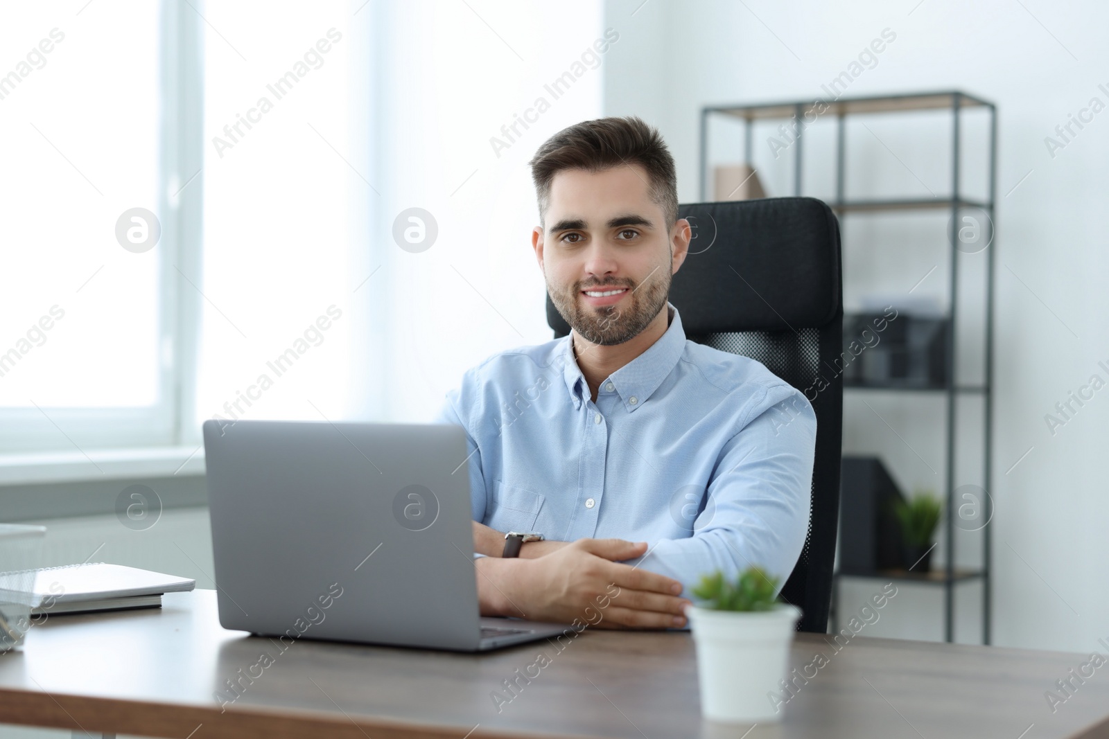 Photo of Happy young programmer working with laptop in office