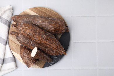 Photo of Whole and cut cassava roots on white tiled table, top view. Space for text