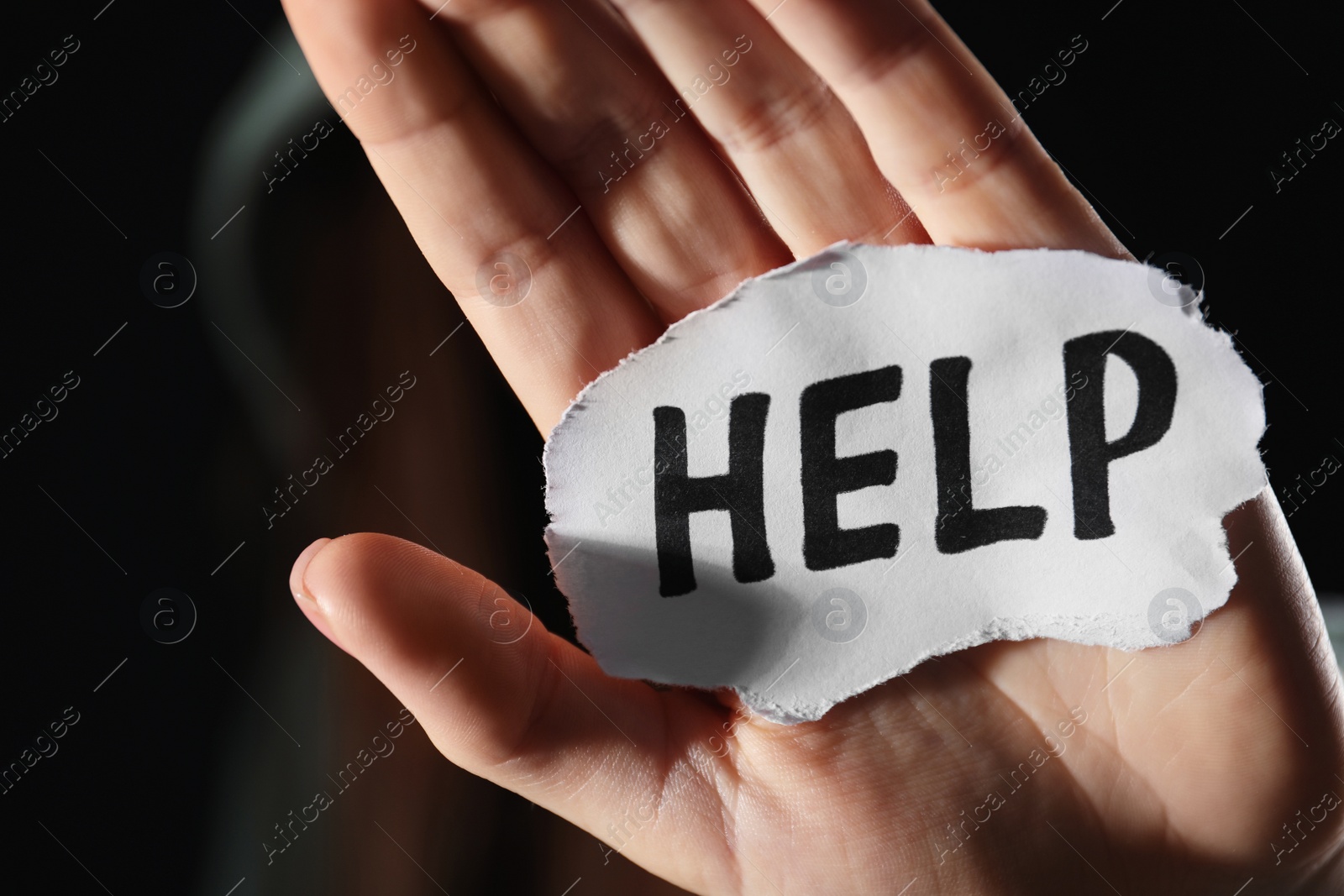 Photo of Woman holding piece of paper with word Help on black background, closeup. Domestic violence concept