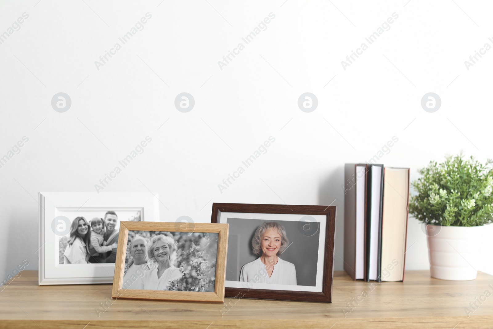 Photo of Framed photos on cabinet near white wall. Space for text