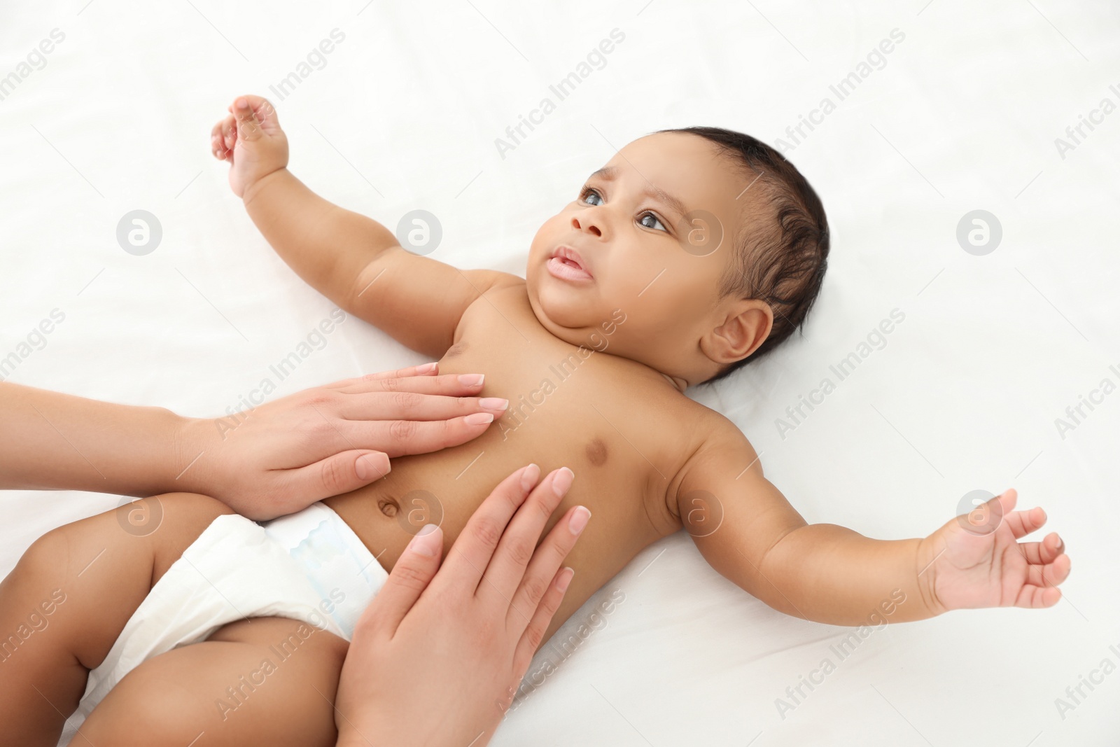 Photo of Mother and her cute child on white bed. Baby massage and exercises