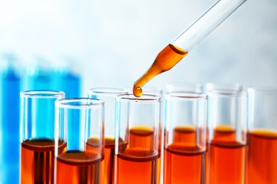 Dropping sample into test tube with orange liquid, closeup