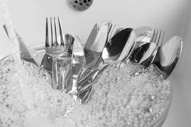 Washing silver spoons, forks and knives under stream of water in kitchen sink, closeup