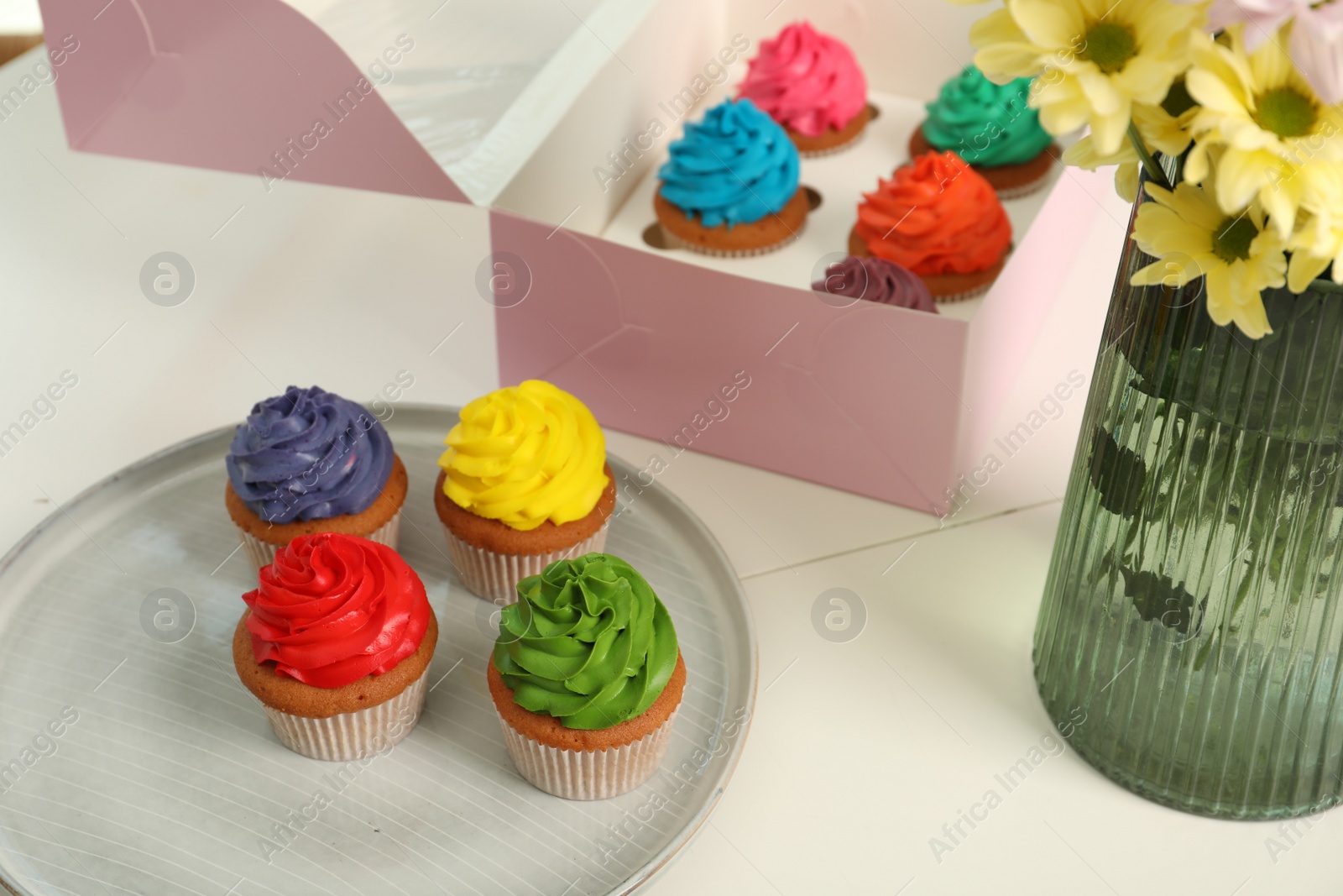 Photo of Delicious colorful cupcakes and beautiful flowers on white table