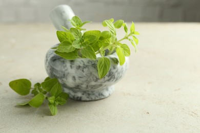 Fresh green oregano in mortar and pestle on light textured table, closeup. Space for text