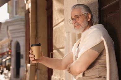 Photo of Handsome senior man standing near building with coffee outdoors, space for text