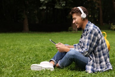 Photo of Student with headphones studying with tablet on green grass in park