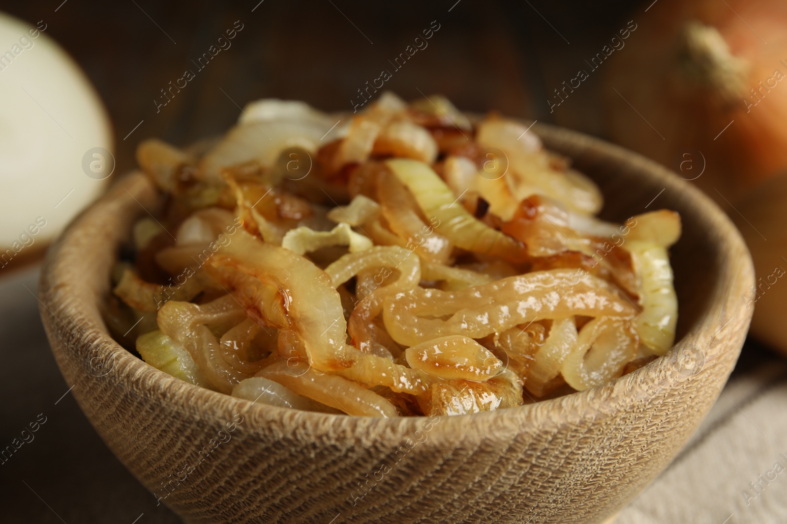 Photo of Tasty fried onion in wooden bowl, closeup