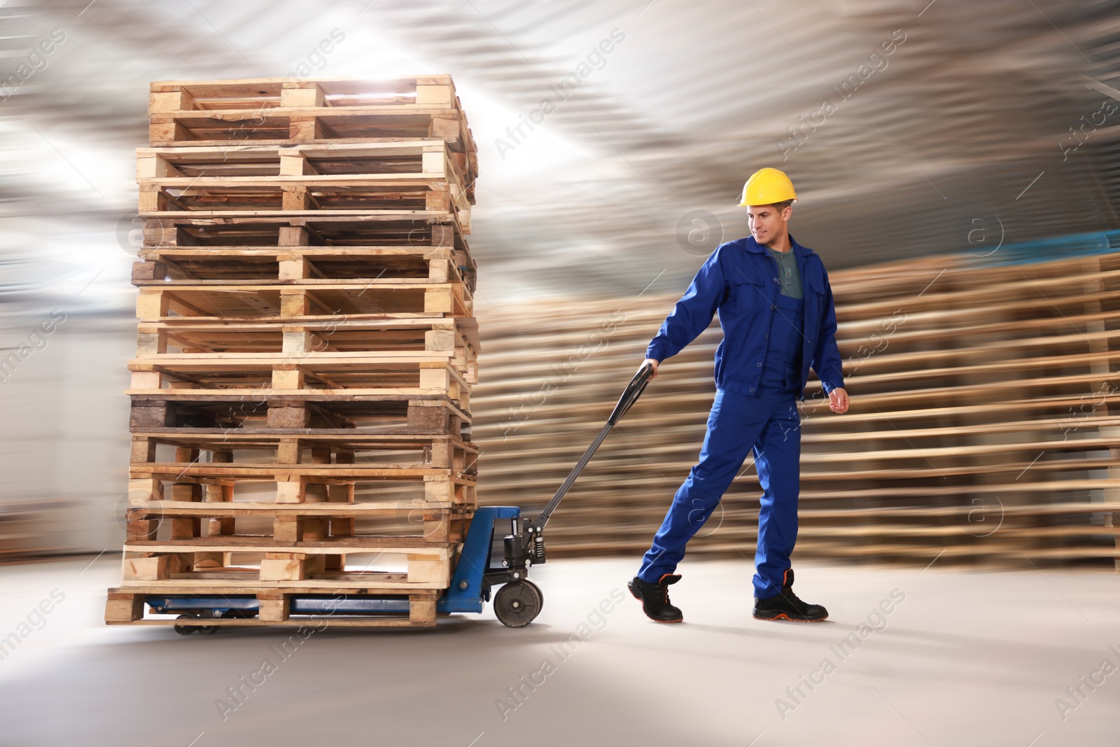 Image of Worker moving wooden pallets with manual forklift in warehouse