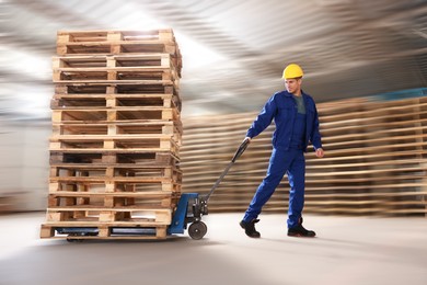 Image of Worker moving wooden pallets with manual forklift in warehouse