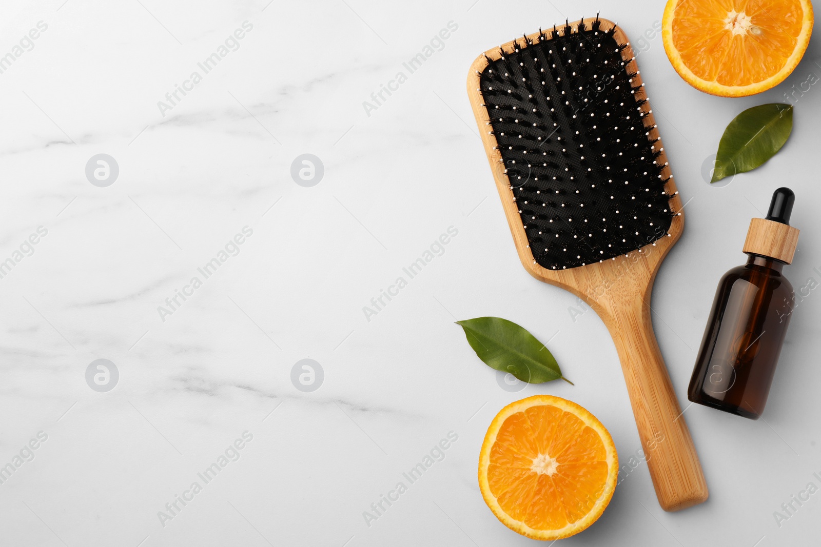 Photo of Wooden hair brush, bottle of essential oil and orange slices on white marble table, flat lay. Space for text