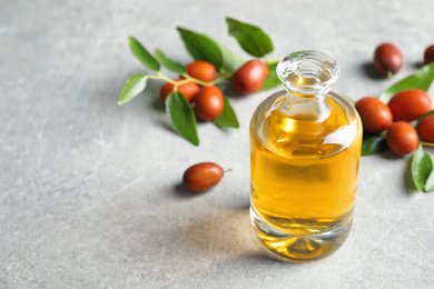 Photo of Jojoba oil in glass bottle and seeds on light grey table