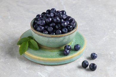 Photo of Tasty fresh bilberries in bowl on light grey marble table