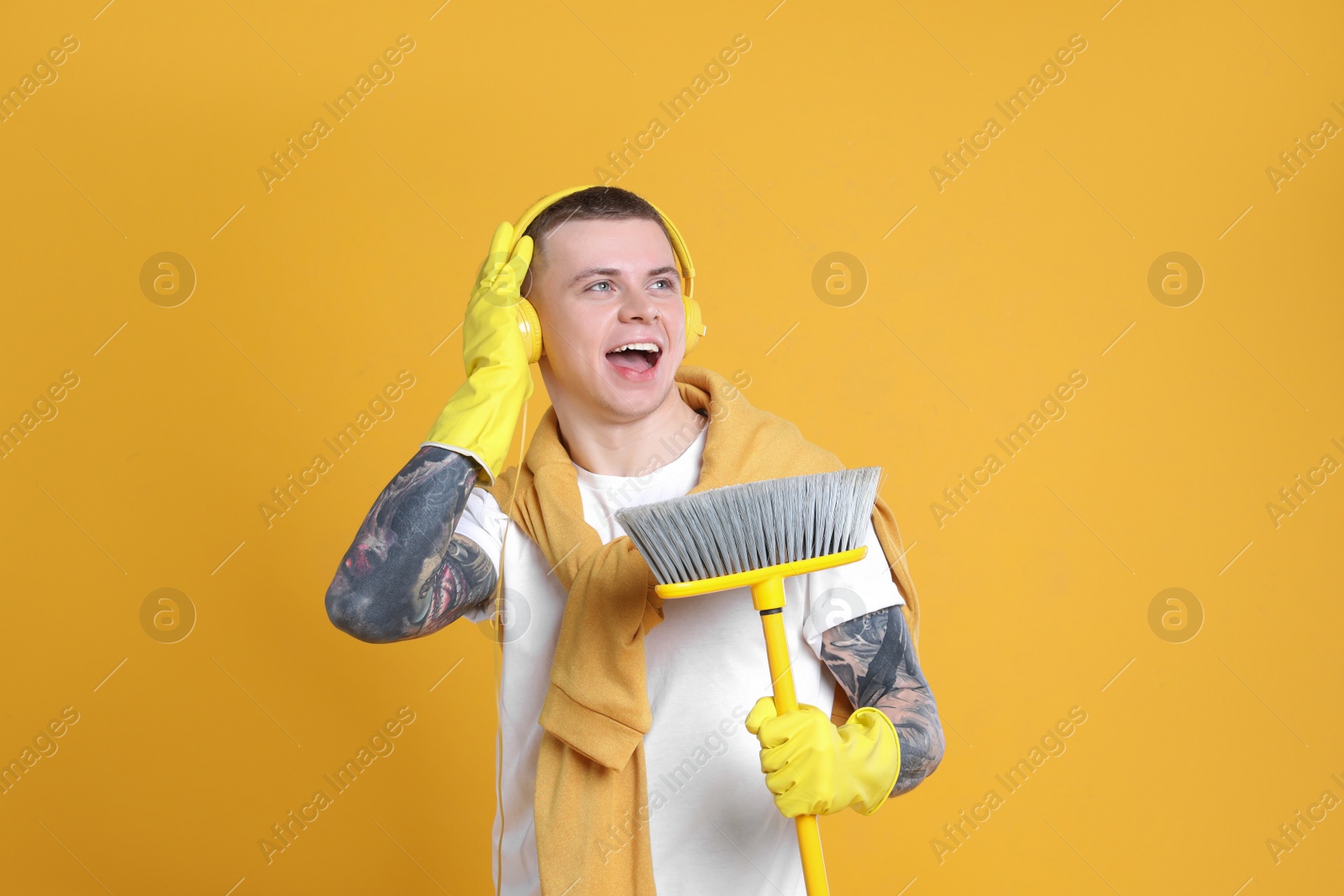 Photo of Handsome young man with floor brush singing on orange background