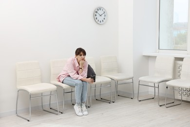 Photo of Woman with cup of drink waiting for appointment indoors