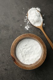 Photo of Baking powder in bowl and spoon on grey textured table, top view