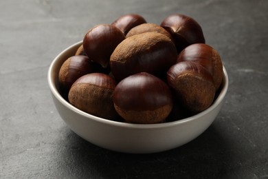 Photo of Roasted edible sweet chestnuts in bowl on grey textured table, closeup