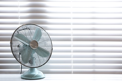 Photo of Modern electric fan on table near window indoors. Space for text