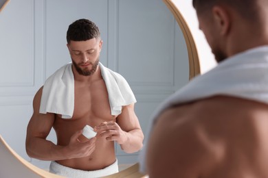 Photo of Handsome man applying body cream near mirror in bathroom