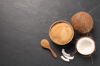 Spoon with coconut sugar, bowl and fruits on dark textured table, flat lay. Space for text