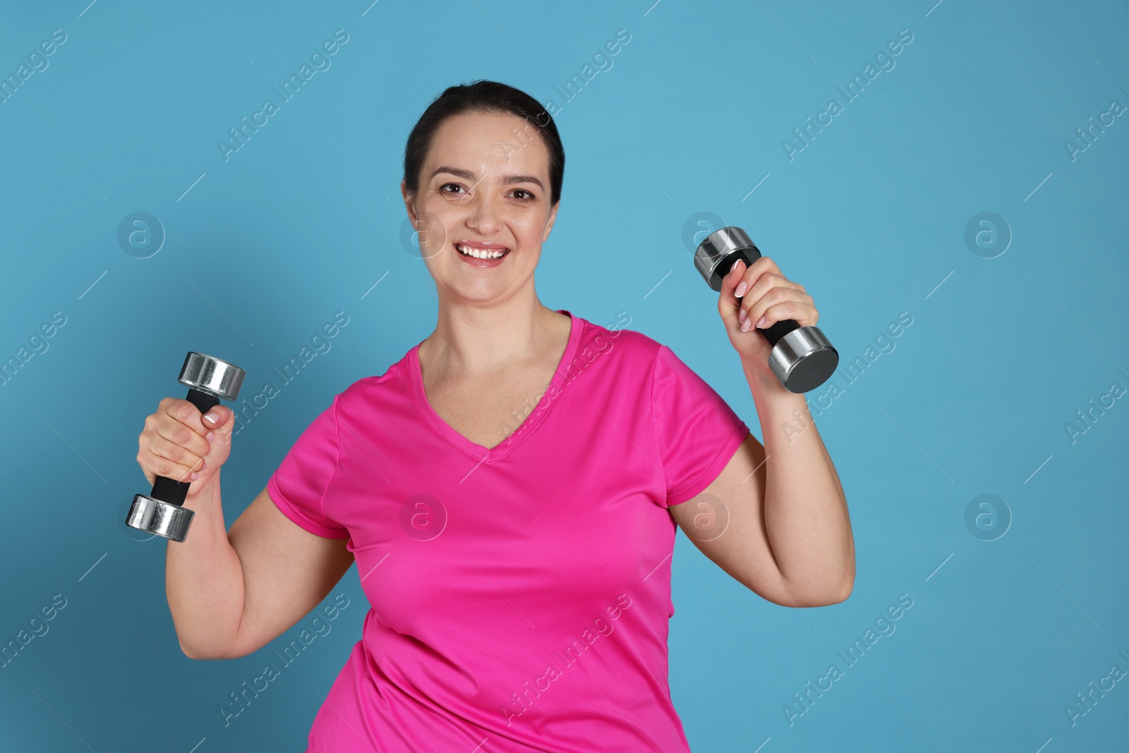 Photo of Happy overweight woman doing exercise with dumbbells on light blue background