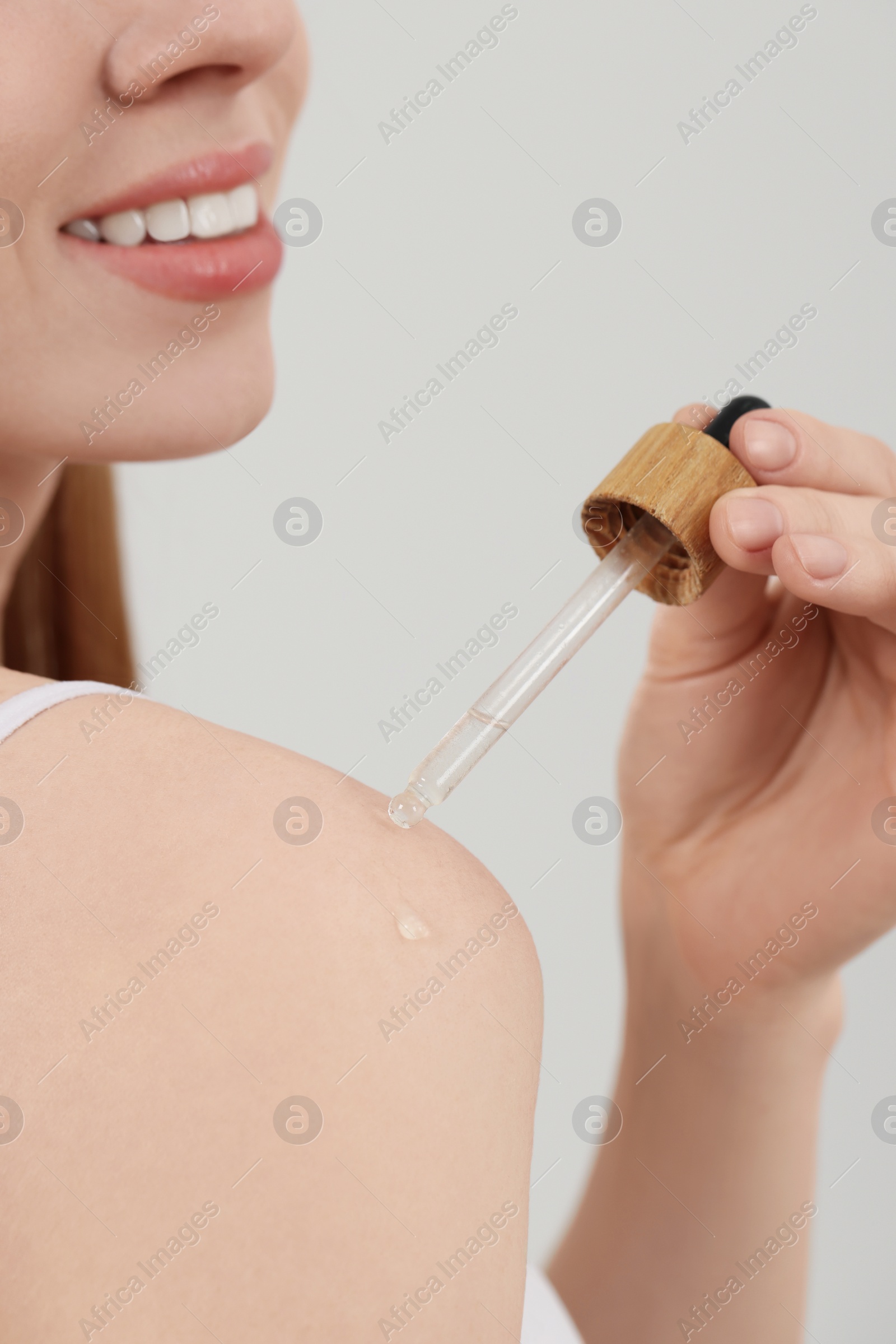 Photo of Woman applying essential oil onto shoulder on light background, closeup