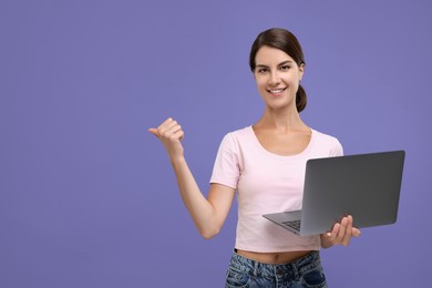 Photo of Special promotion. Happy woman with laptop pointing at something on violet background, space for text