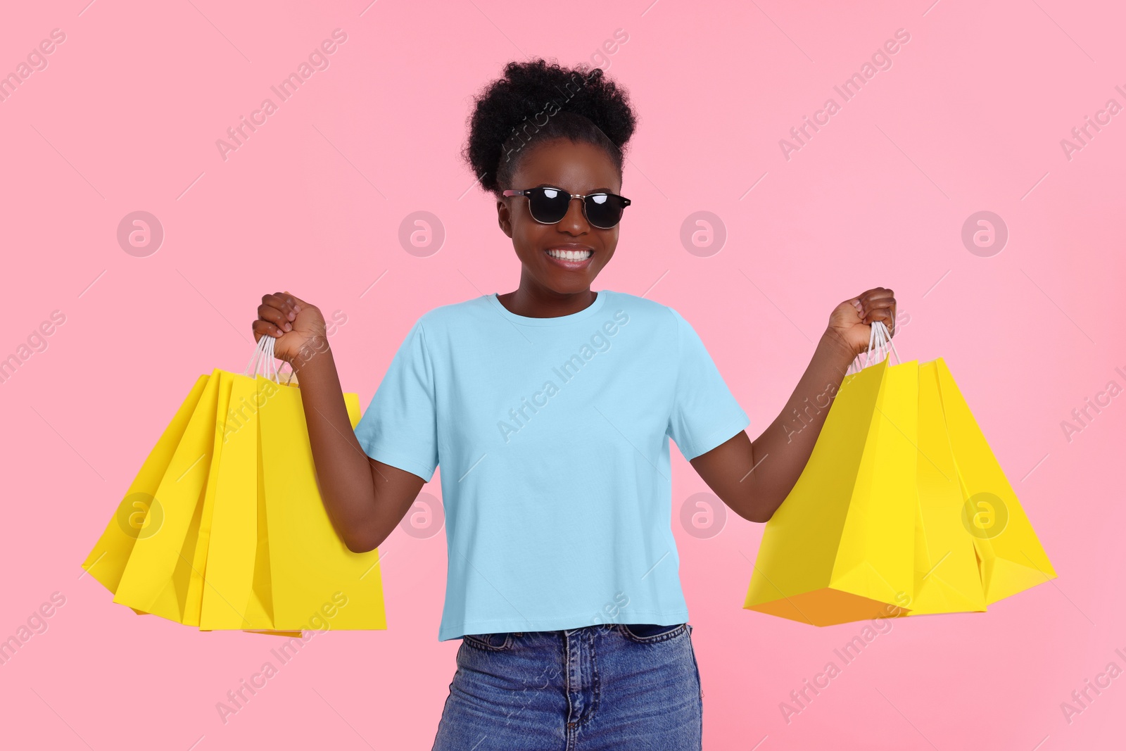 Photo of Happy young woman in stylish sunglasses with shopping bags on pink background