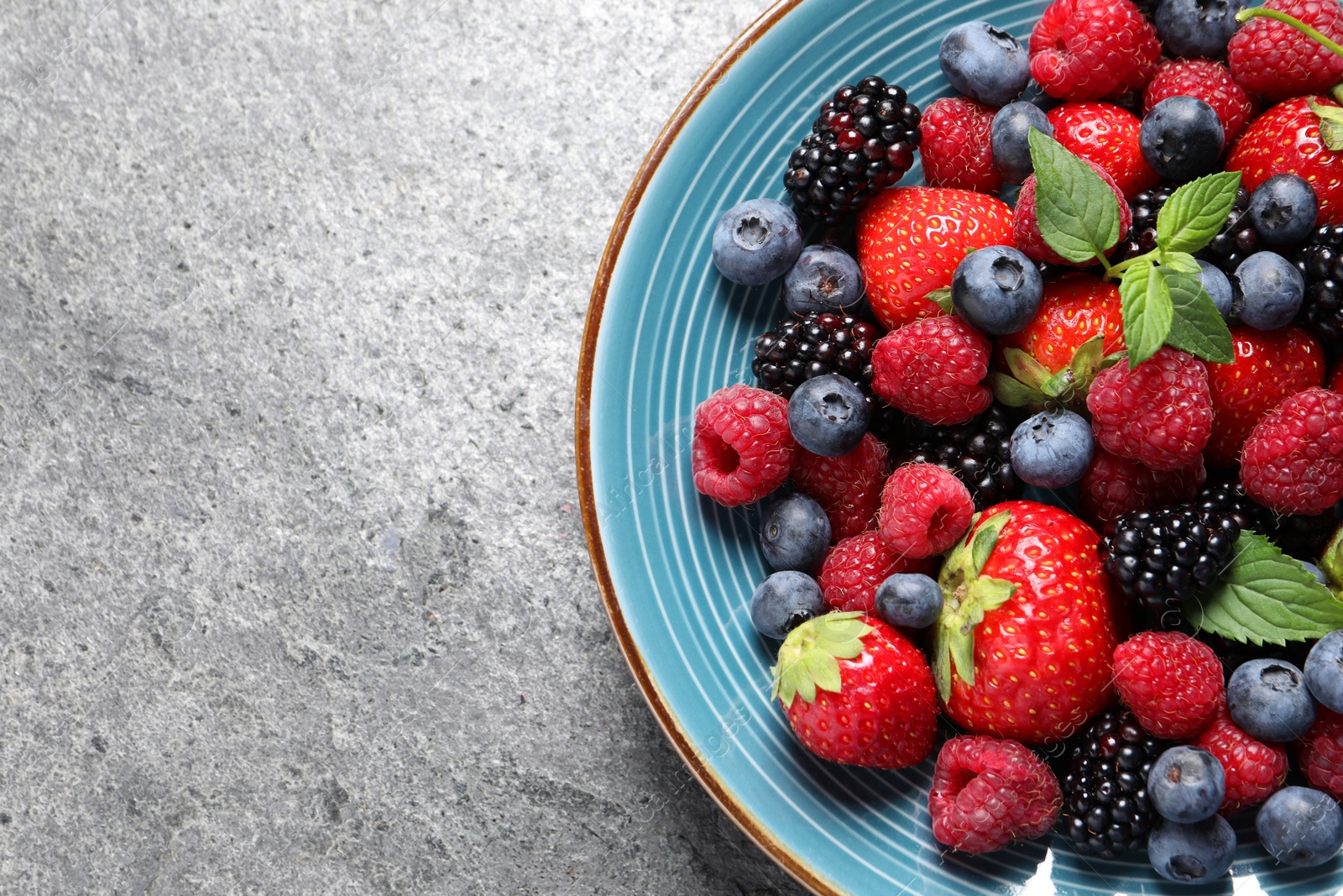 Photo of Many different fresh ripe berries in plate on grey table, top view. Space for text