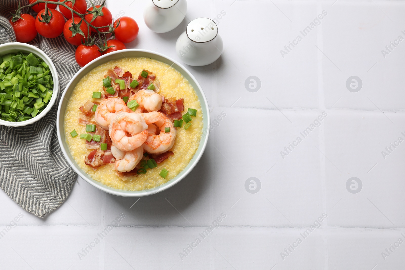Photo of Fresh tasty shrimps, bacon, grits and green onion in bowl on white tiled table, flat lay. Space for text