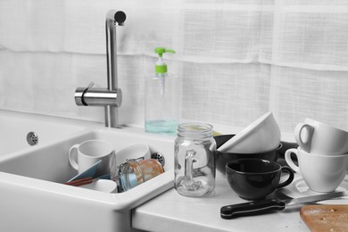 Many dirty utensils and dishware on countertop in messy kitchen