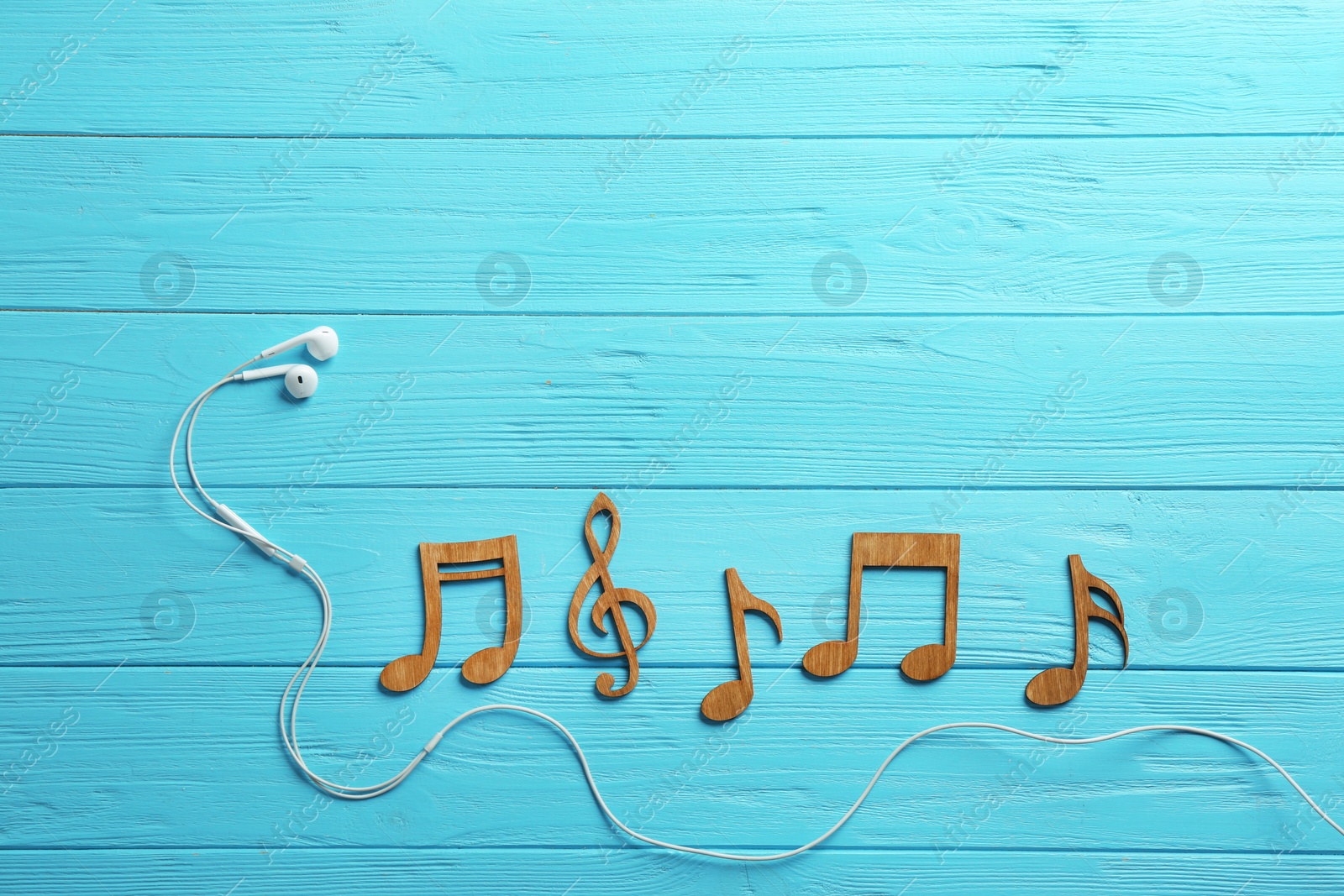 Photo of Earphones and music notes on wooden background, flat lay. Space for text