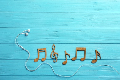 Earphones and music notes on wooden background, flat lay. Space for text