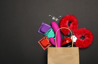 Shopping bag and different sex toys on black background, flat lay. Space for text