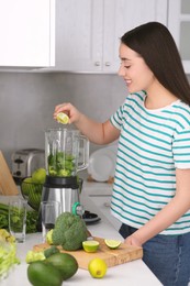 Beautiful young woman adding lime into blender with ingredients for smoothie in kitchen