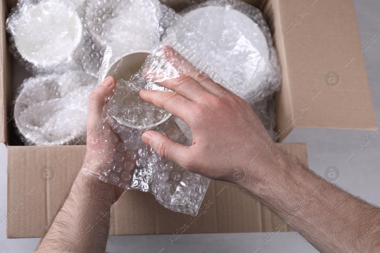 Photo of Man covering ceramic dishware with bubble wrap, closeup