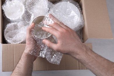 Photo of Man covering ceramic dishware with bubble wrap, closeup