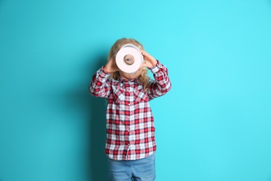 Photo of Cute little girl looking through toilet paper roll on color background