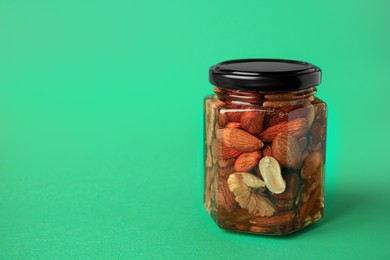 Jar with different tasty nuts and honey on green background, space for text