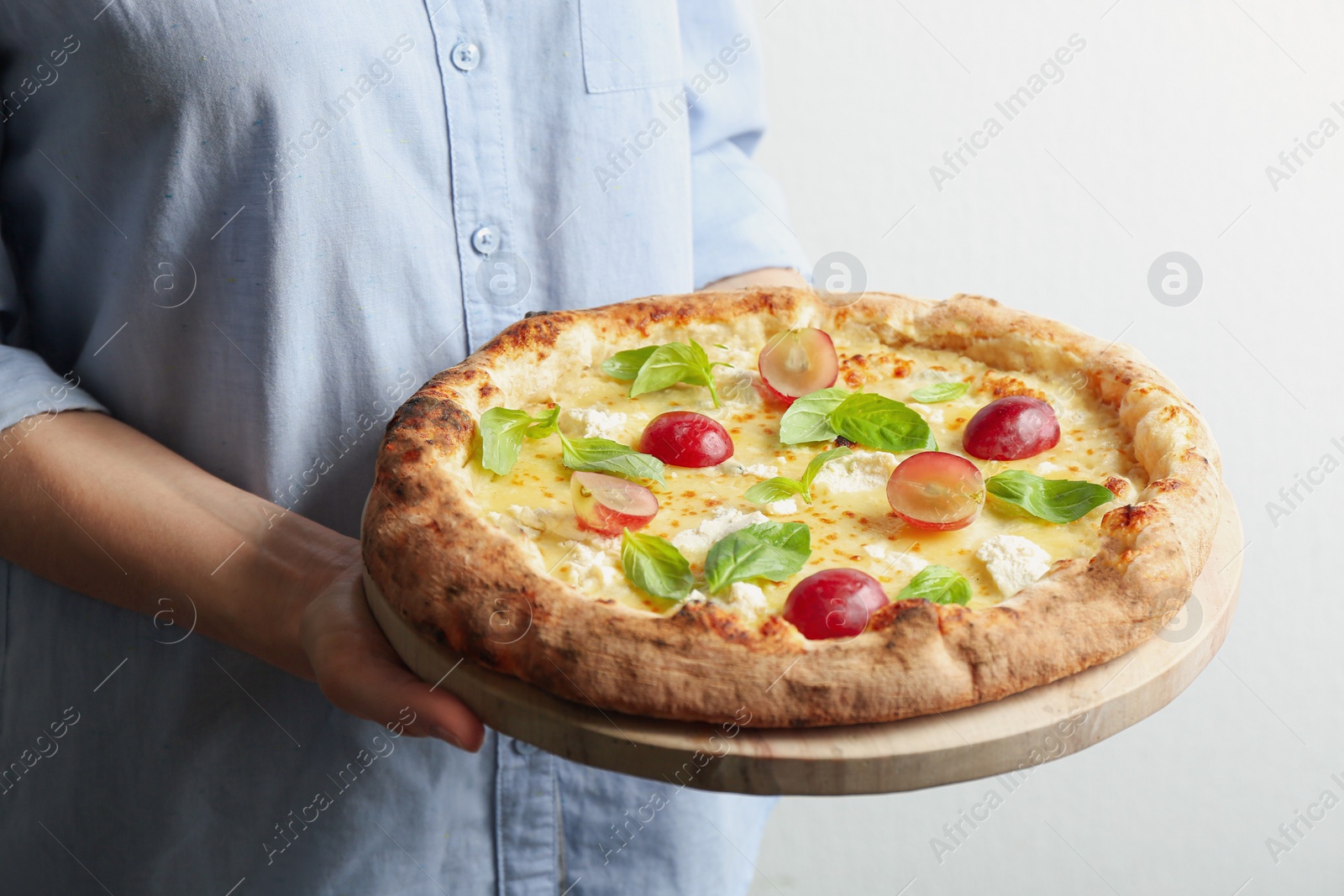 Photo of Woman holding delicious cheese pizza with grapes and basil on light background, closeup