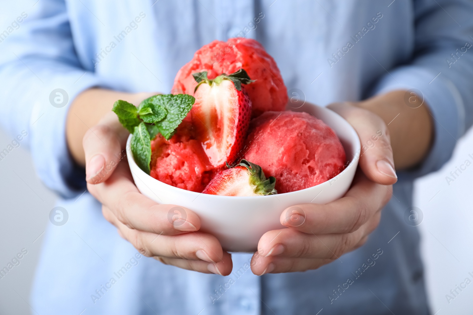 Photo of Woman holding bowl full of delicious ice cream and strawberries, closeup