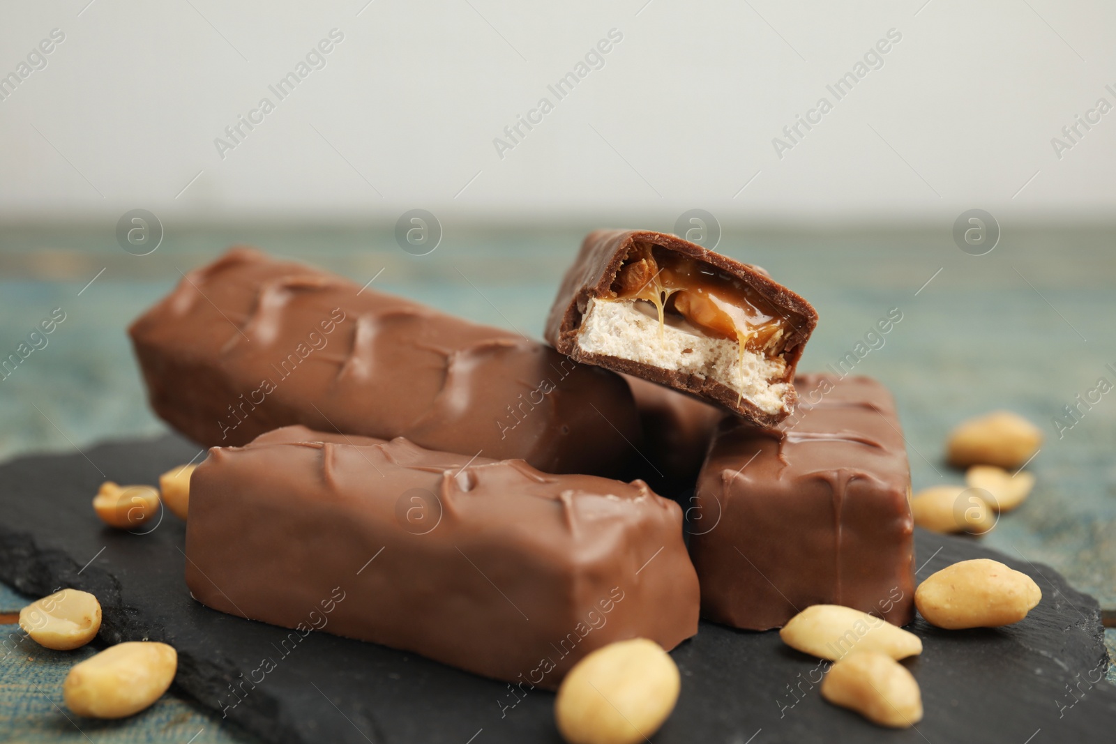 Photo of Slate board of chocolate bars with caramel, nuts and nougat on table, closeup