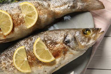 Delicious baked fish and lemon on white wooden table, top view