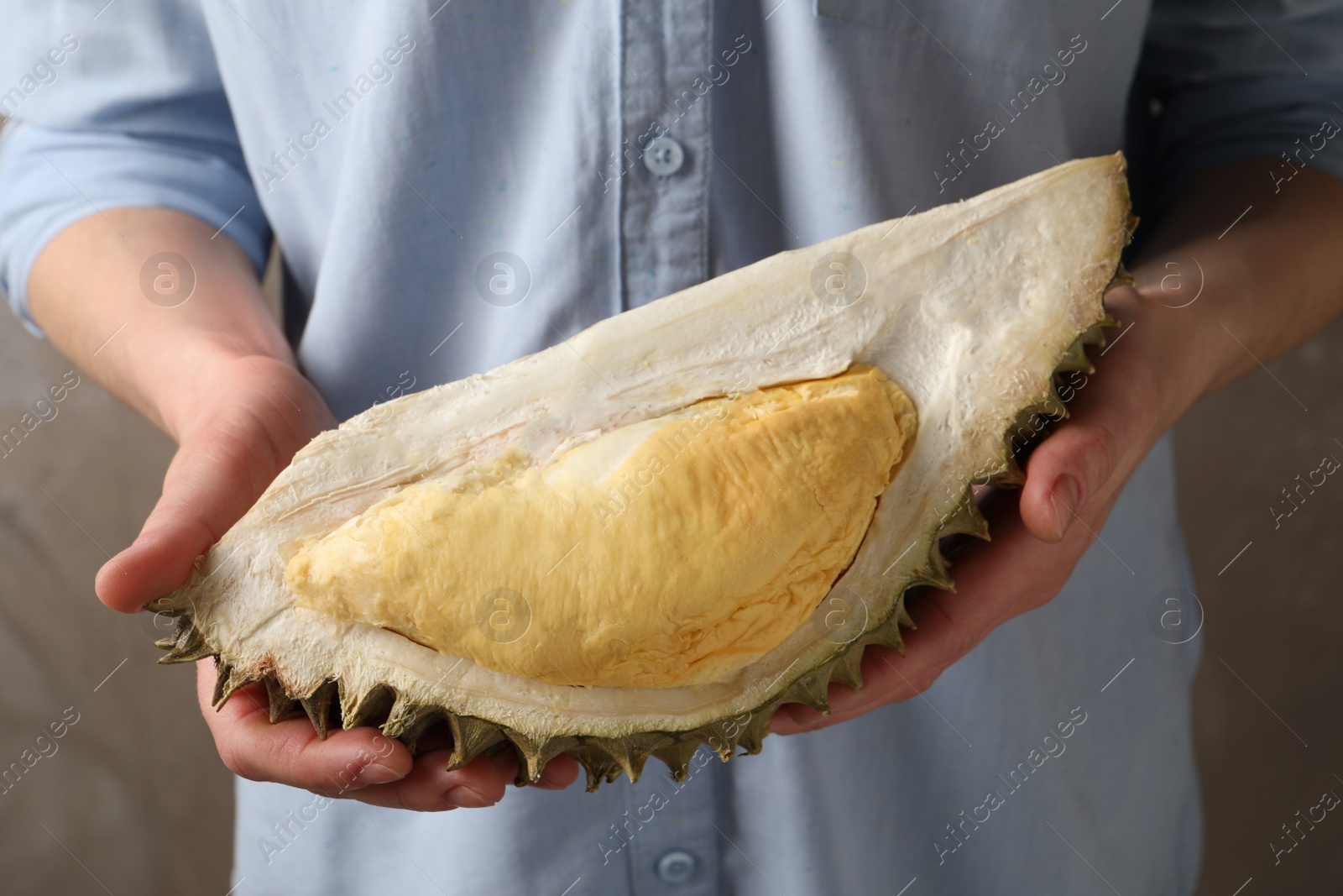 Photo of Woman holding piece of ripe durian fruit on grey background, closeup