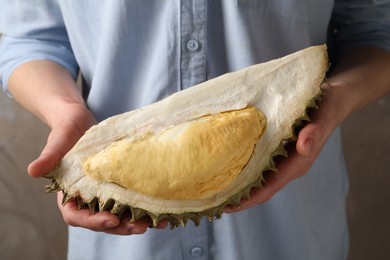 Woman holding piece of ripe durian fruit on grey background, closeup