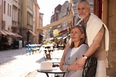 Affectionate senior couple sitting in outdoor cafe, space for text