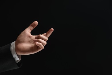 Man holding something in hand on black background, closeup. Space for text