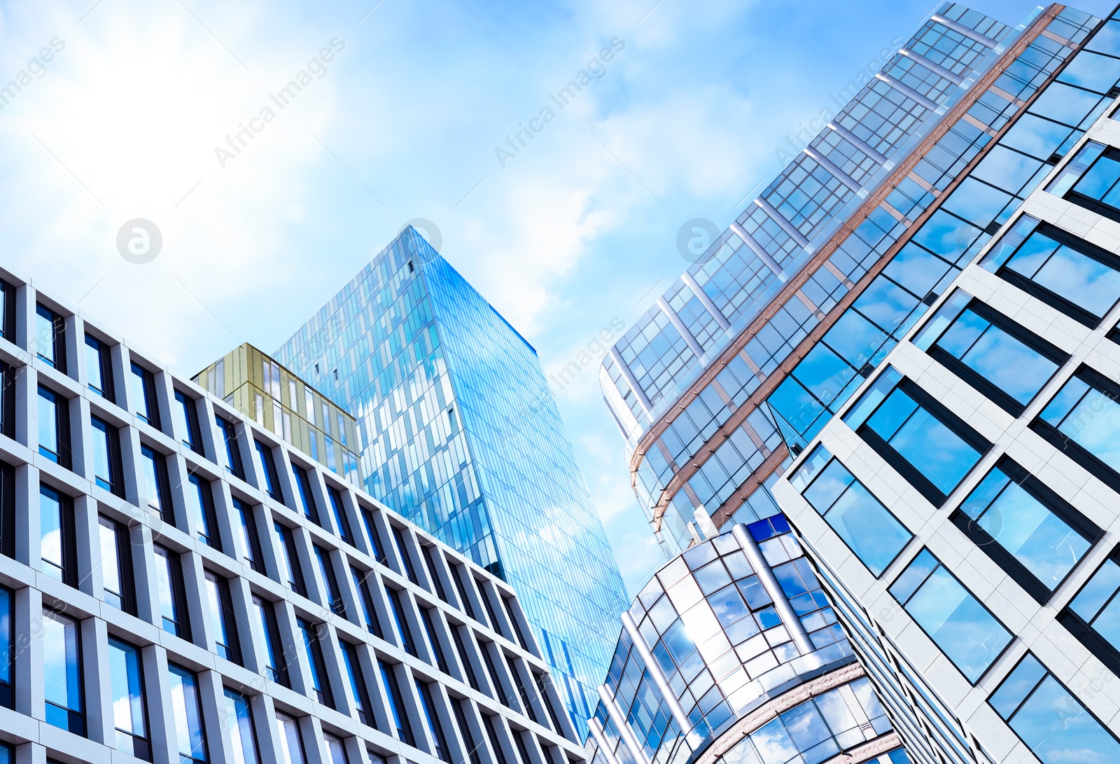 Image of Beautiful blue sky with clouds reflecting in windows of modern buildings. Low angle view